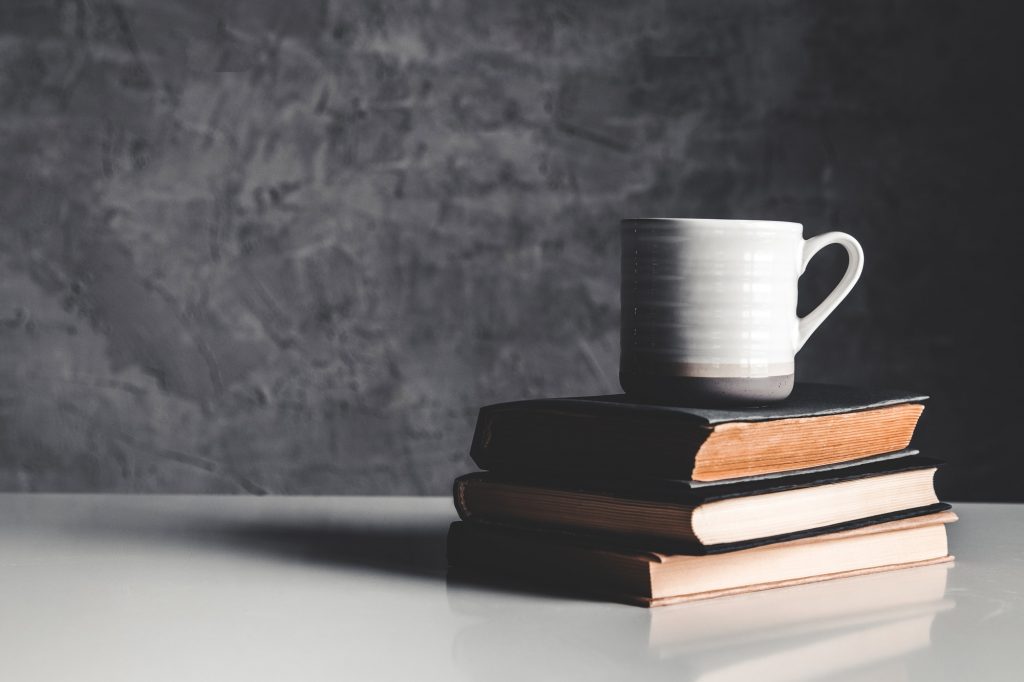 A cup of coffee on stack of books on grey background